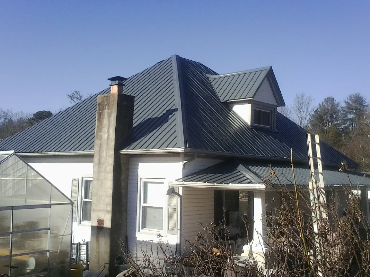 Dark blue standing seam metal roof on a white farmhouse with dormer in Creal Springs