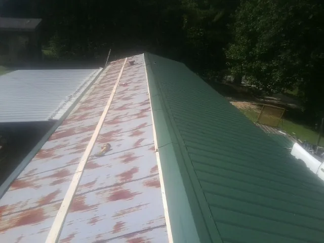 Old rusted panels beside newly installed green metal roofing — Wind Damage Roof Repair by Roofing Brothers in Creal Springs