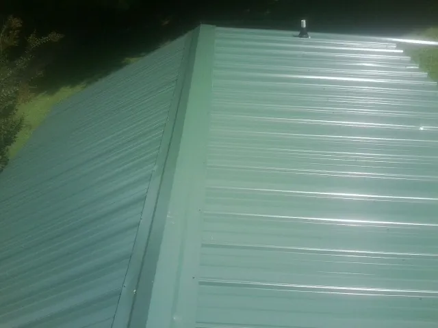 New green metal panels meeting at the ridge of a roof — Flat Roof Repair work by our crew in Creal Springs