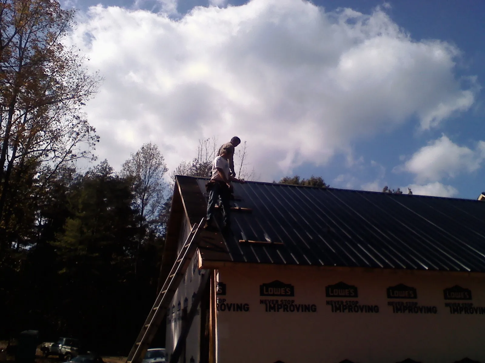 Roofer fastening dark metal panels high against a cloudy sky, from a Roof Inspection job in Creal Springs