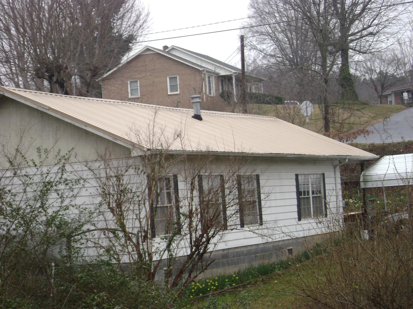 Tan metal roof on a white sided house set into a hillside — Commercial Roofing by Roofing Brothers in Creal Springs